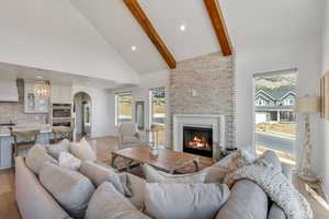Living room featuring arched walkways, high vaulted ceiling, a fireplace, light wood finished floors, and beam ceiling