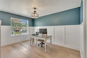 Office space featuring a decorative wall, wainscoting, and light wood-type flooring