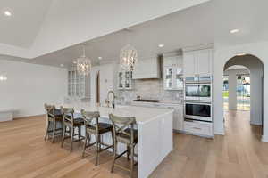 Kitchen with custom range hood, stainless steel double oven, arched walkways, gas cooktop, and backsplash