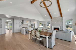 Dining area featuring a chandelier, high vaulted ceiling, beamed ceiling, a brick fireplace, and light wood finished floors