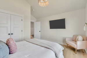 Bedroom with lofted ceiling, light wood-style floors, a chandelier, and a closet