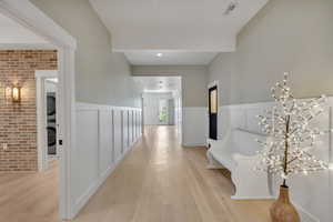 Hall featuring light wood finished floors, wainscoting, brick wall, and a decorative wall