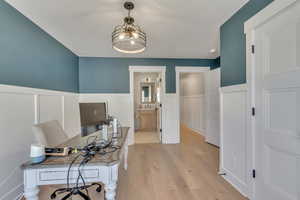 Office with light wood finished floors, a wainscoted wall, and a decorative wall