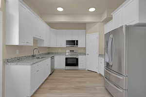 Kitchen featuring stainless steel appliances, white cabinetry, light stone countertops, and light wood-style flooring