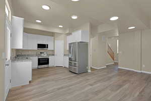 Kitchen featuring appliances with stainless steel finishes, light stone counters, white cabinetry, light wood-style flooring, and recessed lighting