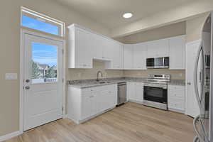 Kitchen with stainless steel appliances, light wood finished floors, white cabinetry, and light stone countertops