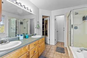 Bathroom with a shower stall, double vanity, light tile patterned floors, a bath, and a walk in closet