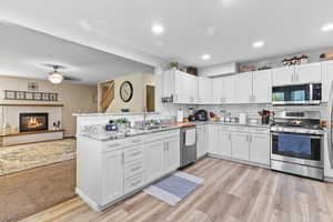 Kitchen with appliances with stainless steel finishes, tasteful backsplash, a glass covered fireplace, light stone counters, and white cabinetry