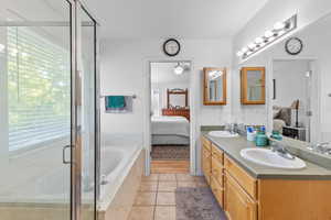 Bathroom featuring ensuite bath, double vanity, a bath, a shower stall, and light tile patterned floors