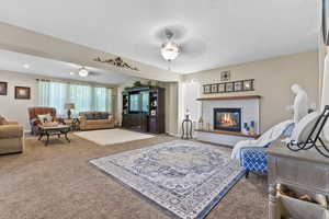 Living room with carpet floors, a ceiling fan, and a glass covered fireplace
