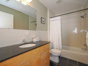 Bathroom featuring tile patterned floors, shower / bath combo with shower curtain, toilet, vanity, and backsplash