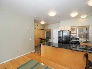 Kitchen featuring black fridge, stainless steel microwave, a sink, a kitchen bar, and light wood finished floors