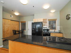 Kitchen with black appliances, a sink, wood finished floors, a kitchen bar, and dark stone counters