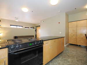 Kitchen featuring electric range, dark countertops, and light brown cabinets