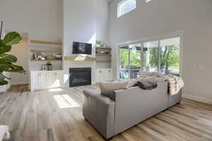 Living room with a towering ceiling, light wood-style flooring, a glass covered fireplace, and built in shelves