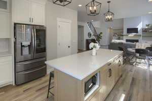 Kitchen featuring stainless steel fridge with ice dispenser, light wood finished floors, a chandelier, open floor plan, and a center island