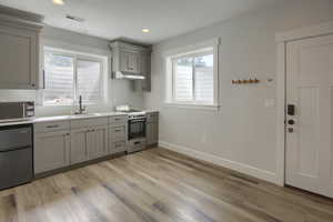 Kitchen with range with gas cooktop, gray cabinetry, under cabinet range hood, stainless steel microwave, and plenty of natural light