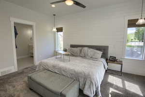 Carpeted bedroom featuring wood walls, multiple windows, a ceiling fan, and ensuite bathroom