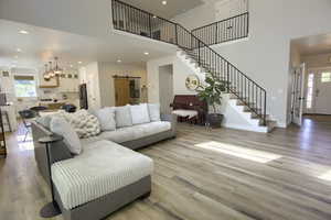Living room featuring a chandelier, a towering ceiling, a barn door, light wood-type flooring, and stairway