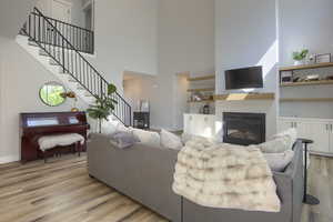 Living room featuring a high ceiling, stairway, light wood-type flooring, and a glass covered fireplace