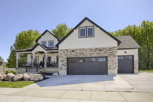 Modern farmhouse with concrete driveway, stone siding, a garage, and covered porch