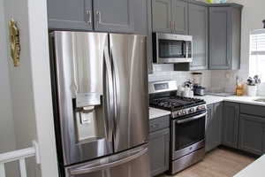 Kitchen with appliances with stainless steel finishes, gray cabinetry, tasteful backsplash, light countertops, and light wood-style flooring