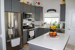 Kitchen featuring appliances with stainless steel finishes, decorative backsplash, light countertops, and gray cabinetry