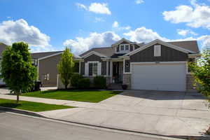 Craftsman-style house featuring board and batten siding, a garage, a front yard, and stone siding