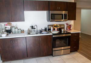 Kitchen with stainless steel appliances, dark brown cabinets, and light tile patterned flooring