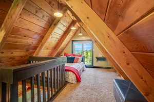 Bedroom with carpet, access to exterior, lofted ceiling, and wooden walls