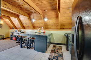 Kitchen featuring black appliances, wood ceiling, light tile patterned floors, a breakfast bar, and decorative light fixtures