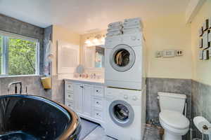 Laundry area with estacked washer and dryer, tile walls, tile patterned flooring, and a wainscoted wall