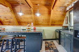 Kitchen featuring black gas range oven, wood ceiling, light tile patterned floors, a breakfast bar area, and decorative light fixtures