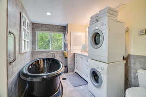 Full bath with tile walls, stacked washer / drying machine, a freestanding tub, and a textured ceiling