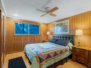 Bedroom featuring wood finished floors, ornamental molding, wood walls, and ceiling fan