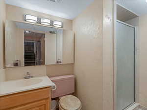 Bathroom featuring a textured wall, a textured ceiling, a shower stall, and vanity