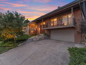 Front of property featuring brick siding, an attached garage, concrete driveway, and a balcony