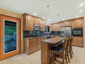 Kitchen featuring black appliances, light tile patterned floors, dark stone countertops, decorative backsplash, and recessed lighting