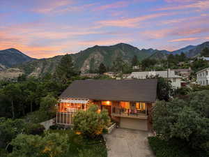 Back of property at dusk with concrete driveway, a mountain view, a sunroom, a chimney, and a garage