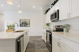 Kitchen with stainless steel appliances, light wood-style floors, light countertops, white cabinetry, and hanging light fixtures