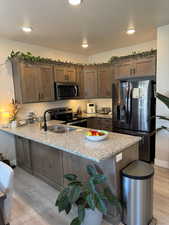 Kitchen featuring stainless steel appliances, a peninsula, light wood-style flooring, light stone counters, and a textured ceiling