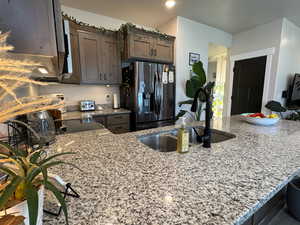 Kitchen featuring stainless steel fridge with ice dispenser, light stone counters, and dark brown cabinetry