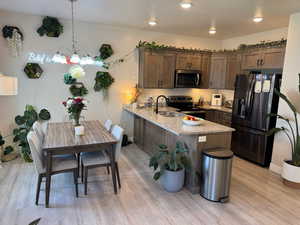Kitchen with appliances with stainless steel finishes, a peninsula, light wood-type flooring, light stone counters, and a chandelier