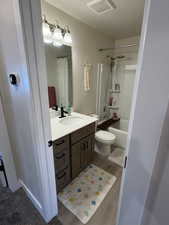 Full bath with vanity, a textured ceiling, shower / bathtub combination with curtain, and wood finished floors
