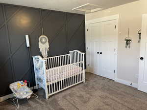 Carpeted bedroom with a crib, a decorative wall, attic access, and a closet