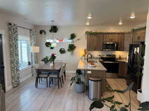 Kitchen featuring appliances with stainless steel finishes, a peninsula, light wood finished floors, light stone counters, and a textured ceiling