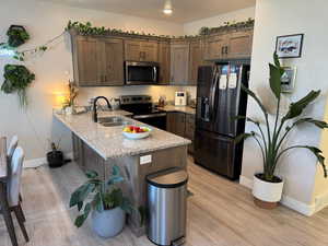 Kitchen featuring appliances with stainless steel finishes, a peninsula, light wood-style flooring, and light stone counters