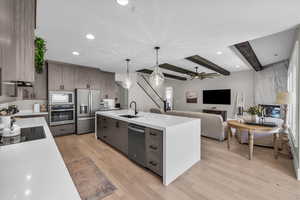 Kitchen with stainless steel appliances, light countertops, light wood finished floors, beamed ceiling, and ceiling fan
