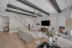 Living area featuring stairway, a tiled fireplace, light wood-style flooring, ceiling fan, and beam ceiling