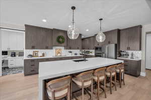 Kitchen featuring appliances with stainless steel finishes, decorative backsplash, a kitchen bar, modern cabinets, and dark brown cabinetry